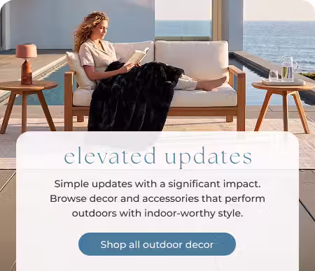 Woman reading on an outdoor loveseat with side tables beside a pool overlooking the coast.
