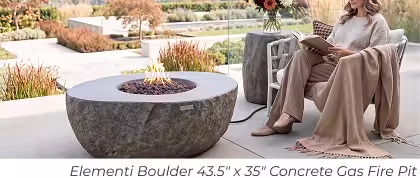 Elementi Boulder concrete gas fire pit with lava rock beside a woman reading on a modern patio.